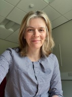 Dr Gow smiling to camera in an office wearing a blue and white checked shirt